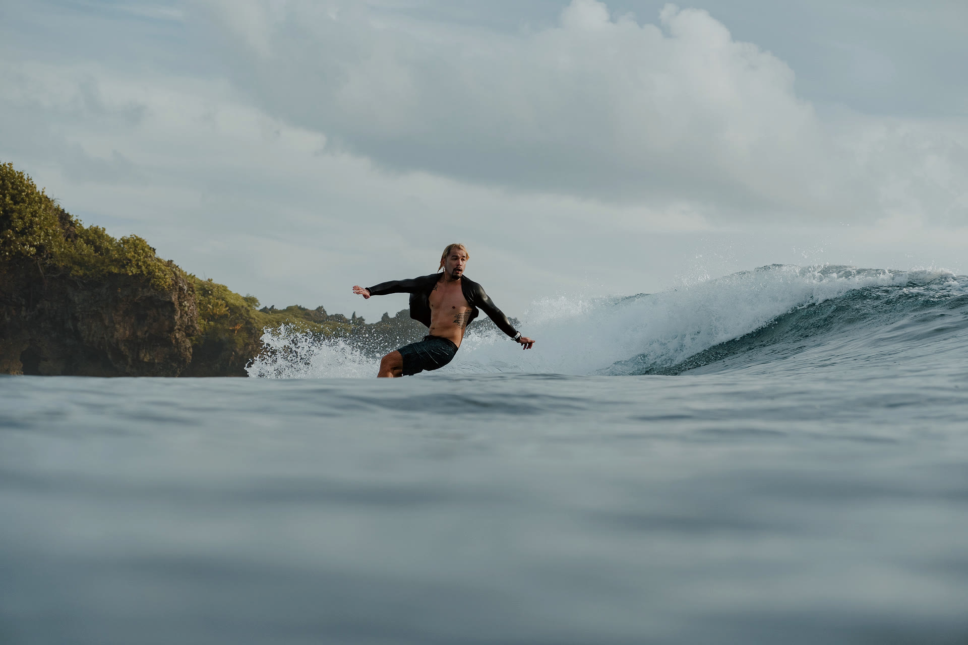 The physician carves a wave with a forested cliff close on the left and dramatic spray on the right. The remote break setting the Field Guide is built for.