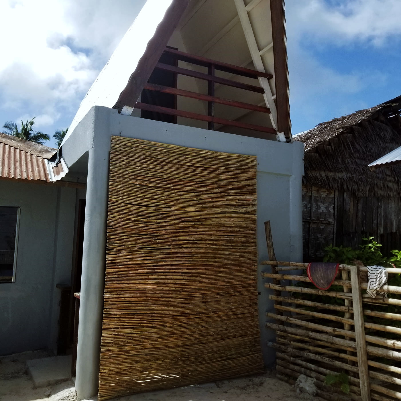A small house in Siargao with a bamboo wall accent, concrete steps, thatched roof attached, and a palm tree visible. The first place Dr. Divinagracia stayed after arriving on the island.