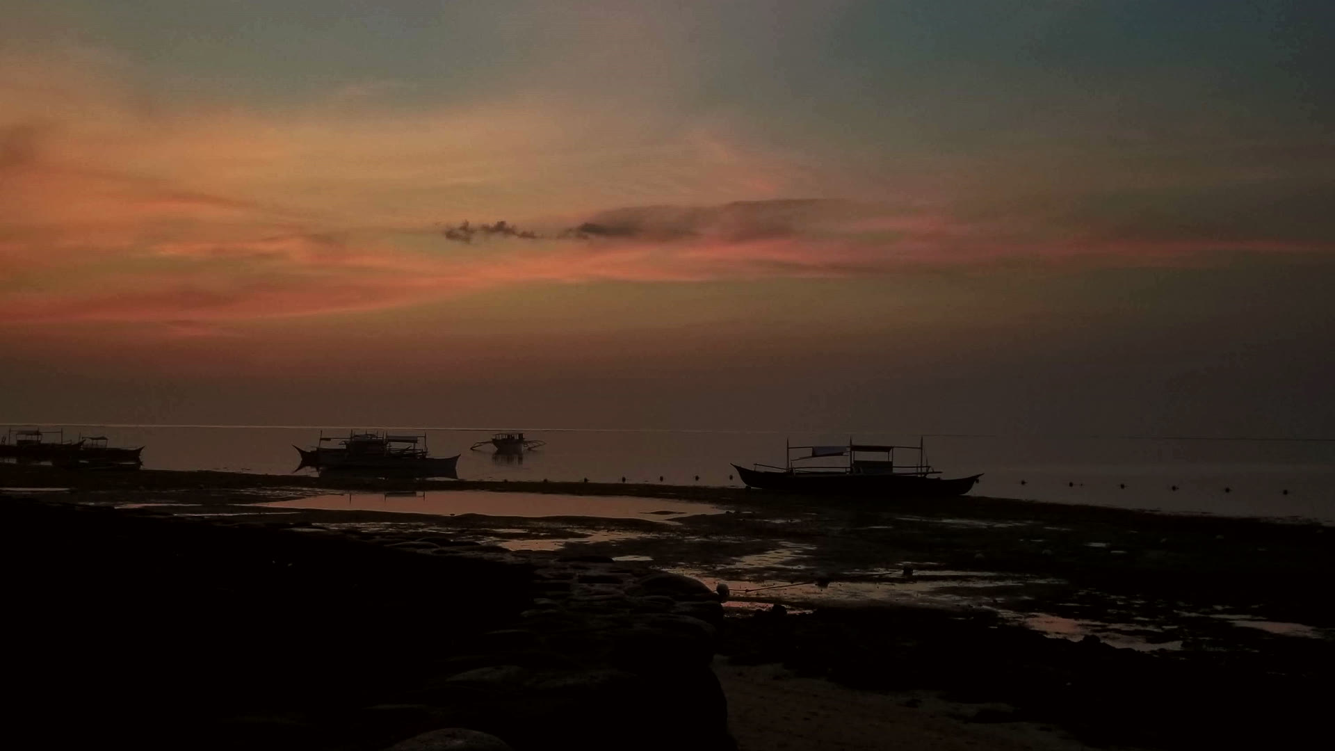 Filipino banca outrigger boats silhouetted on a tidal flat at sunset. Pastel sky over still water.